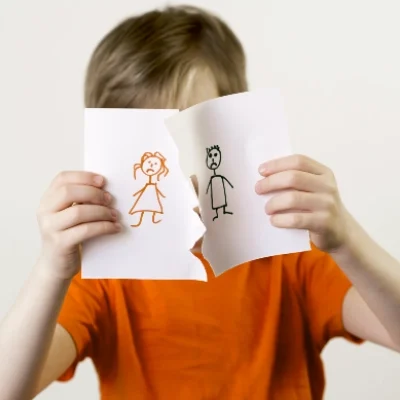 A child in an orange shirt tears apart a drawing of two stick figures, symbolizing separation—expert investigation for sensitive cases.
