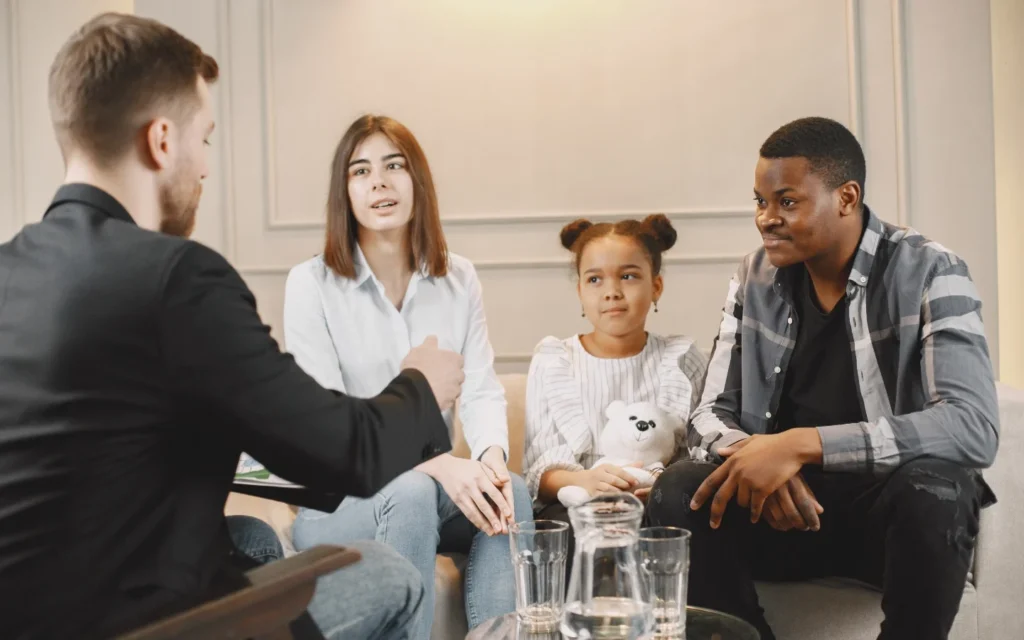 Four people, including a young girl with a stuffed toy, talk in a bright room—Metro Detective Agency ensures your family’s safety.