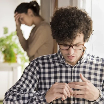 A man in a checkered shirt examines a ring thoughtfully, while an upset woman leans against a wall—capturing suspicion and secrets.