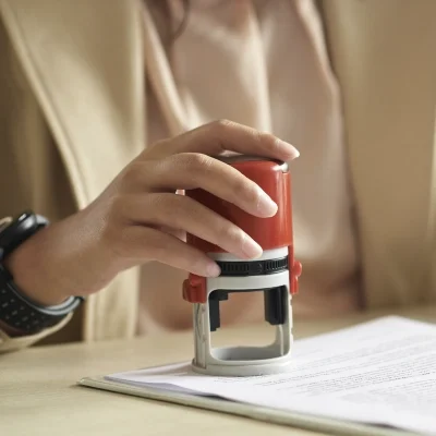 A licensed private investigator presses a red rubber stamp onto official documents, ensuring authenticity and legal compliance at their desk.