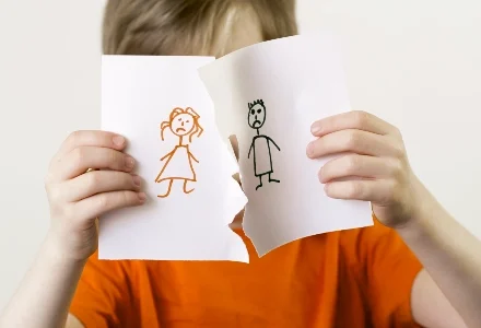 Child in an orange shirt holding two torn papers with stick figure drawings, symbolizing family separation—private investigator services.