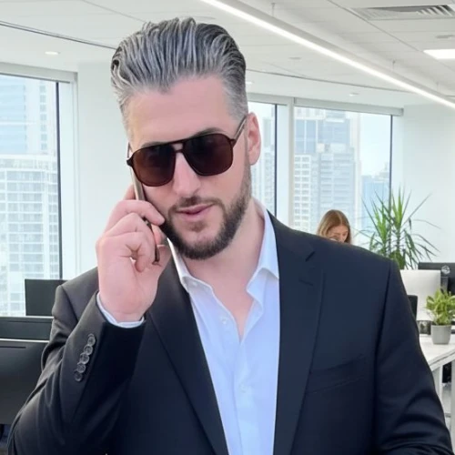 A private investigator in a black suit and sunglasses talks on his phone in a modern office with big windows and cityscape views.