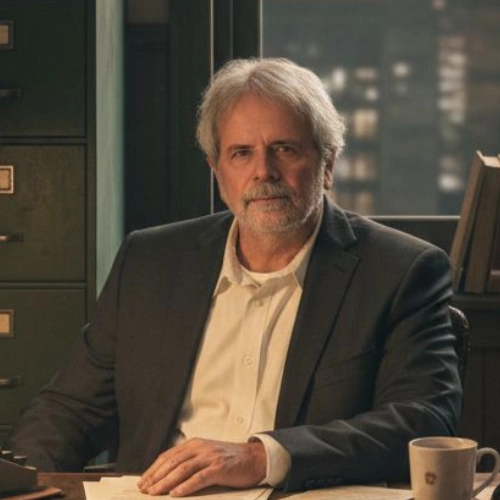 An experienced private investigator with gray hair and a beard sits at his office desk, surrounded by case files, books, and coffee.