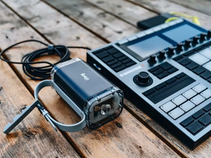 A portable LED lantern and a music production controller with pads and knobs rest on a wooden surface, ideal tools for private investigator gear.
